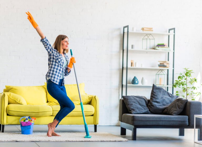 smiling young woman dancing living room with cleaning equipments