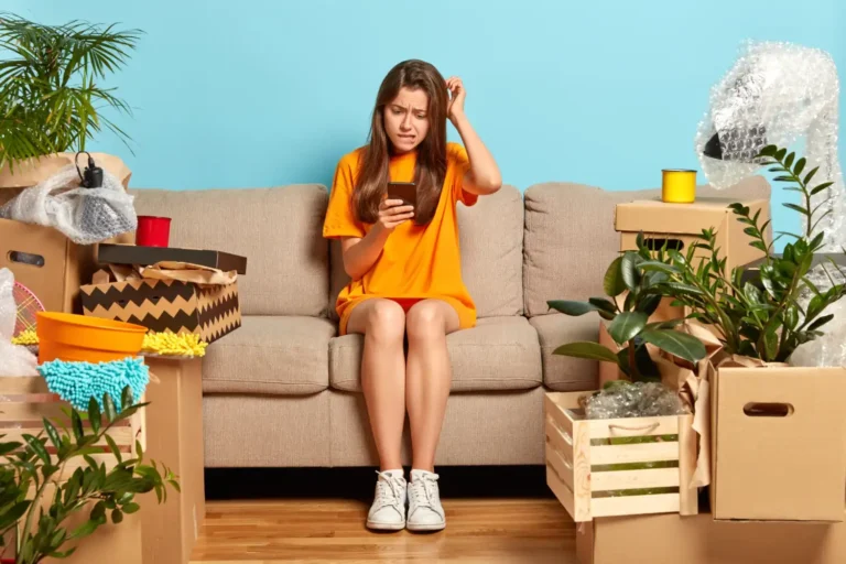 mulher no sofa com preocupacao celular caixas de papelao e plantas mudanca